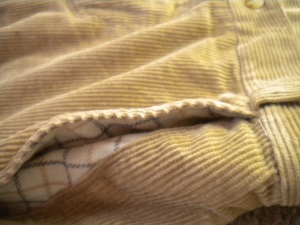 side view of pockets of wide-wale corduroy pants, showing white and blue plaid lining peeking through